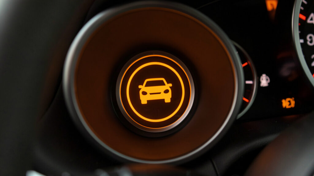 Gros plan sur un voyant orange rond représentant une voiture, allumé sur le tableau de bord d’un véhicule pour signaler un diagnostic.